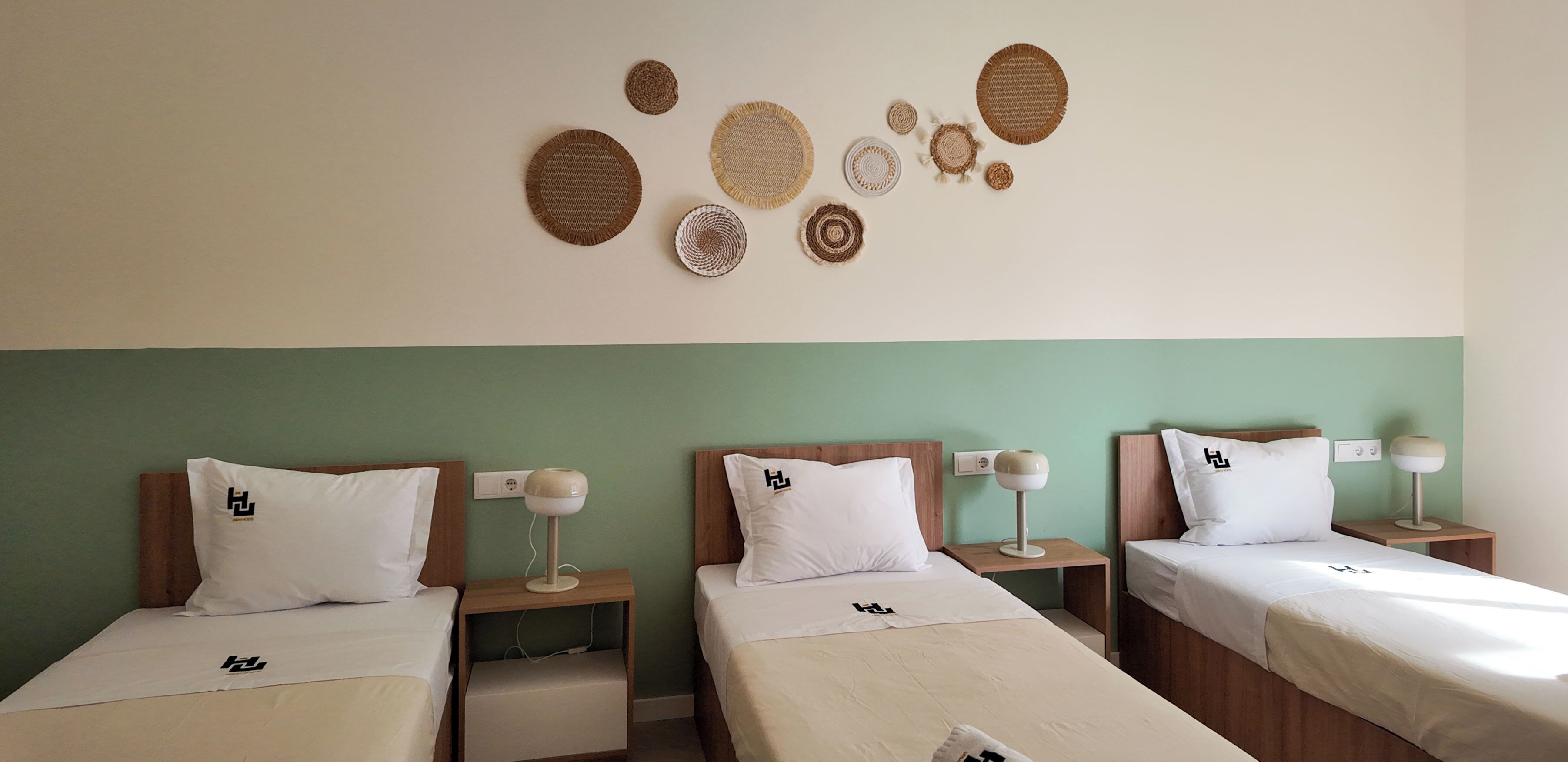 Une chambre d’hôtel avec trois lits simples, chacun doté d’un oreiller blanc et d’une petite table de chevet avec une lampe.