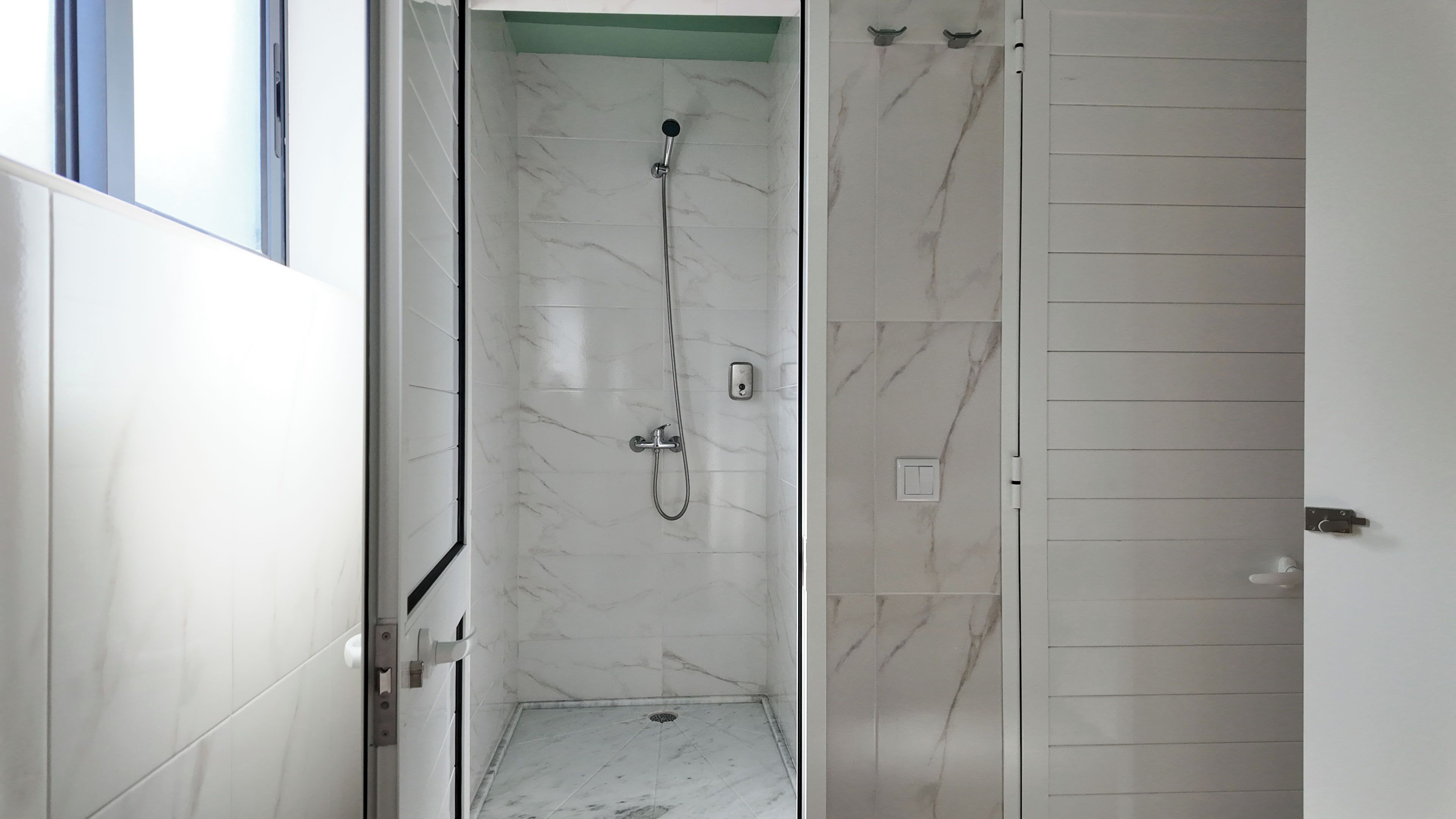 Une salle de bain avec une douche, des murs recouverts de carreaux blancs et une porte.