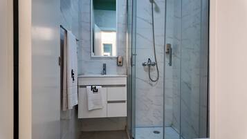 Un baño moderno con cabina de ducha de vidrio, un lavamanos blanco con un espejo encima y una toalla colgada en la pared.
