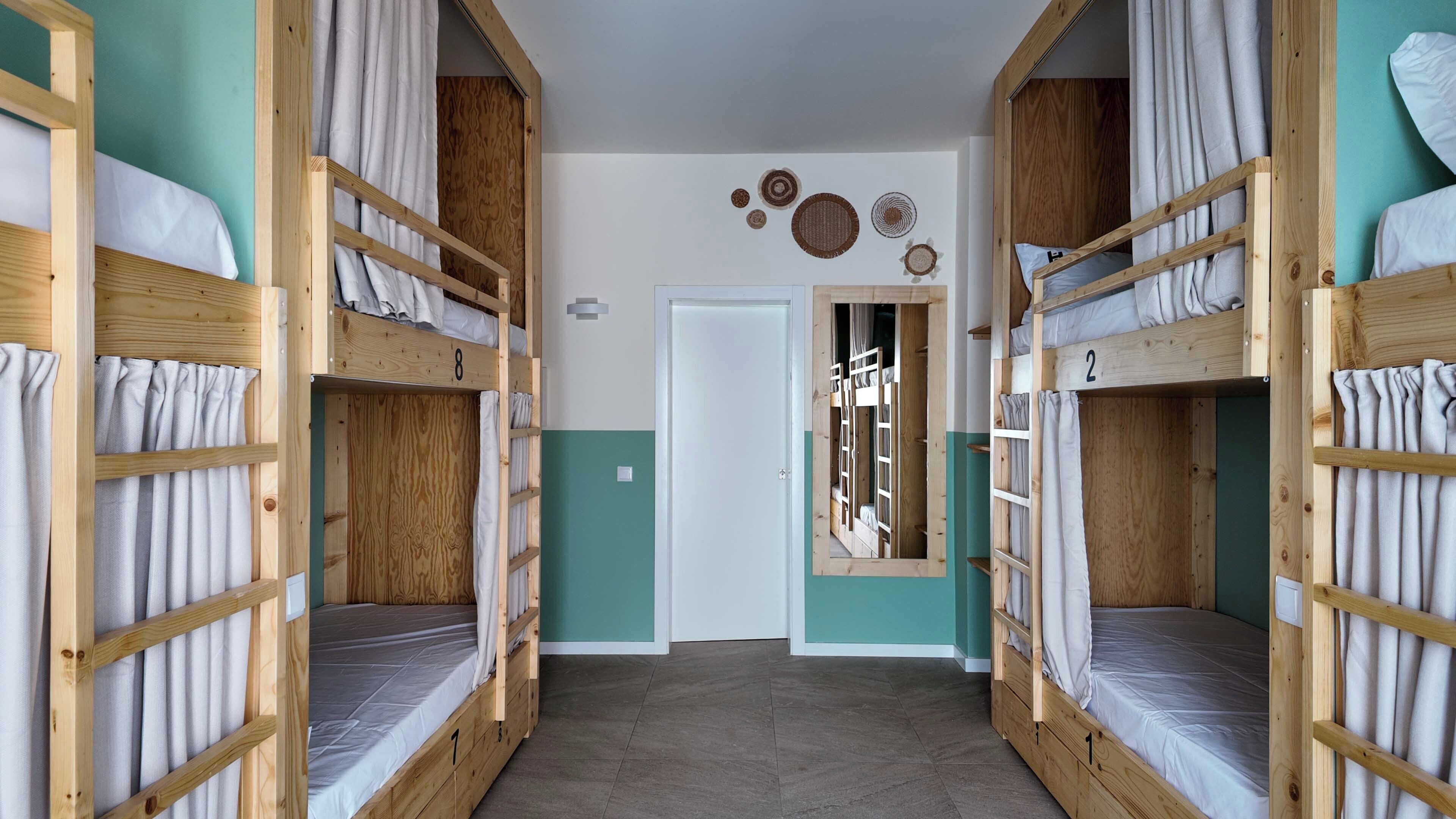 Un pasillo con literas, puertas de habitaciones numeradas y una puerta que da a otra habitación.