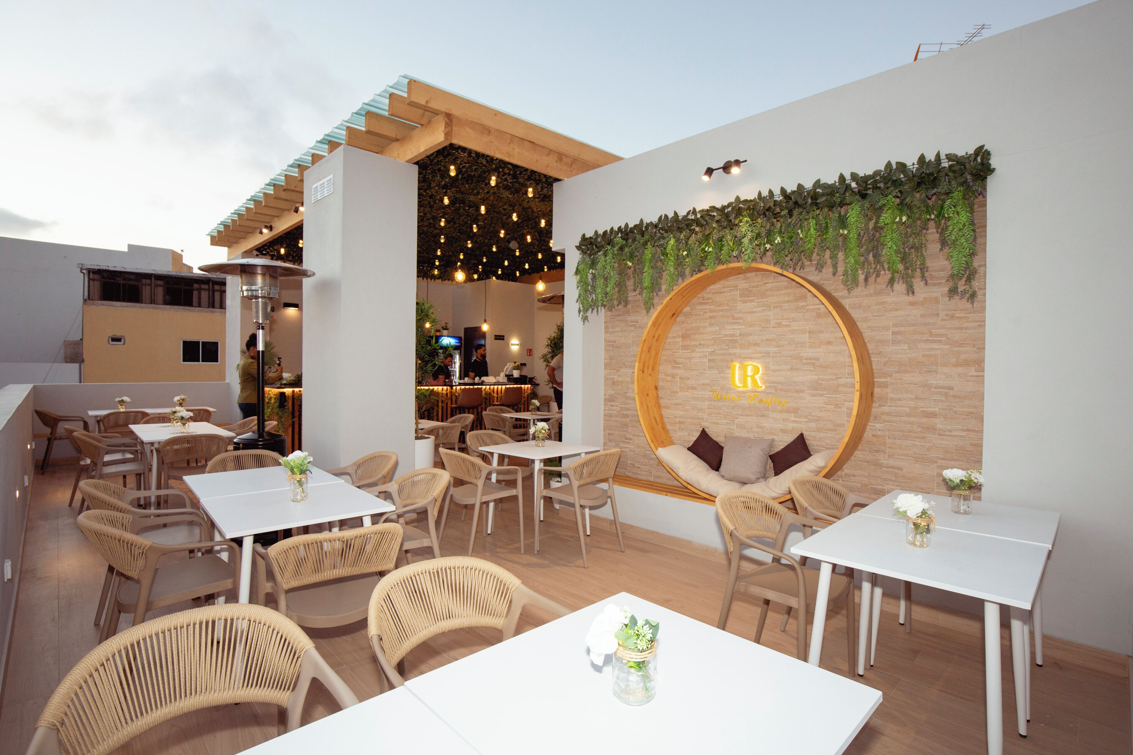 An outdoor seating area with tables and chairs, a circular wall feature with a logo, and a hanging light fixture.