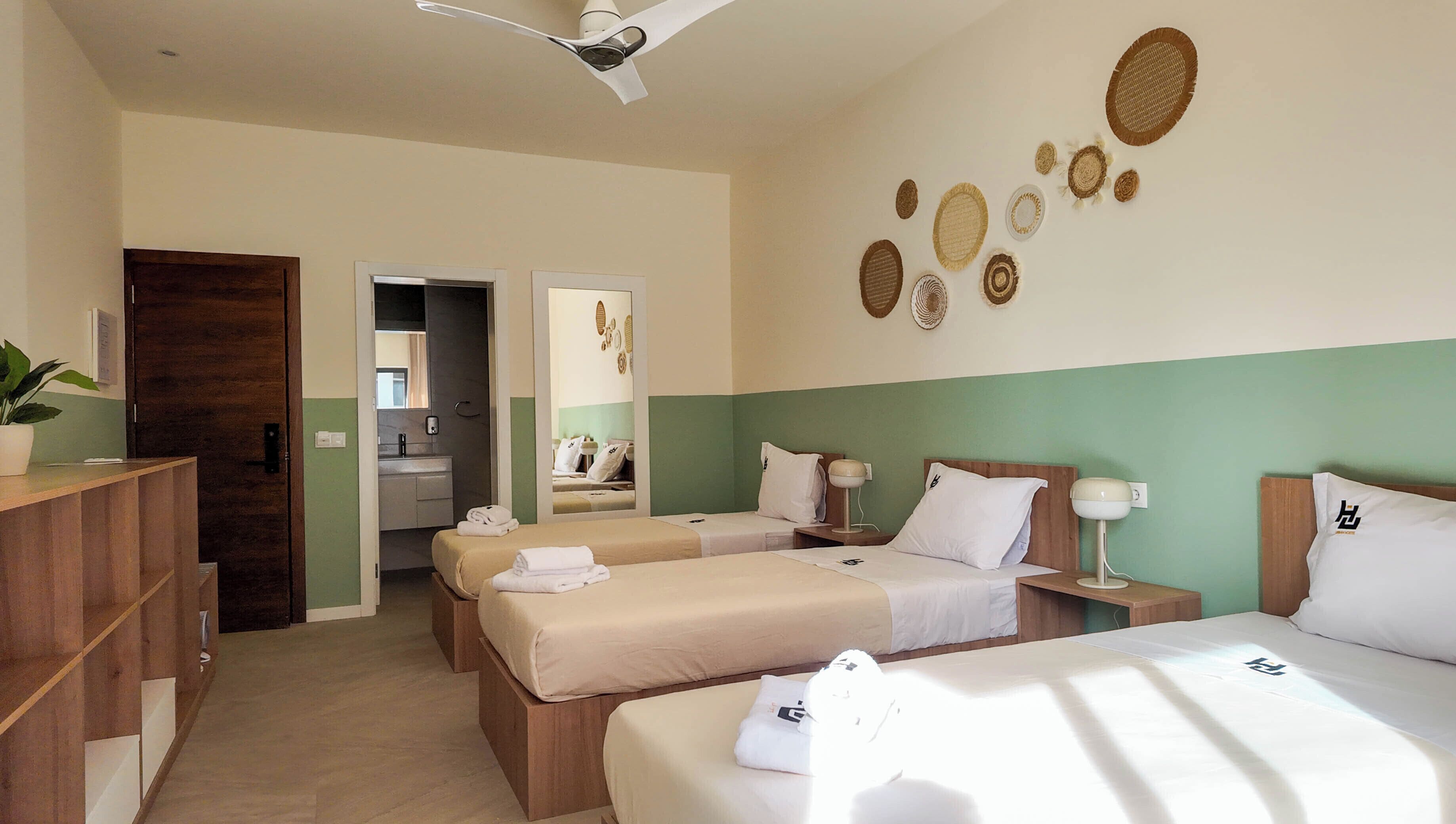 A hotel room with two beds, a desk, a mirror, and a bathroom visible through an open door.