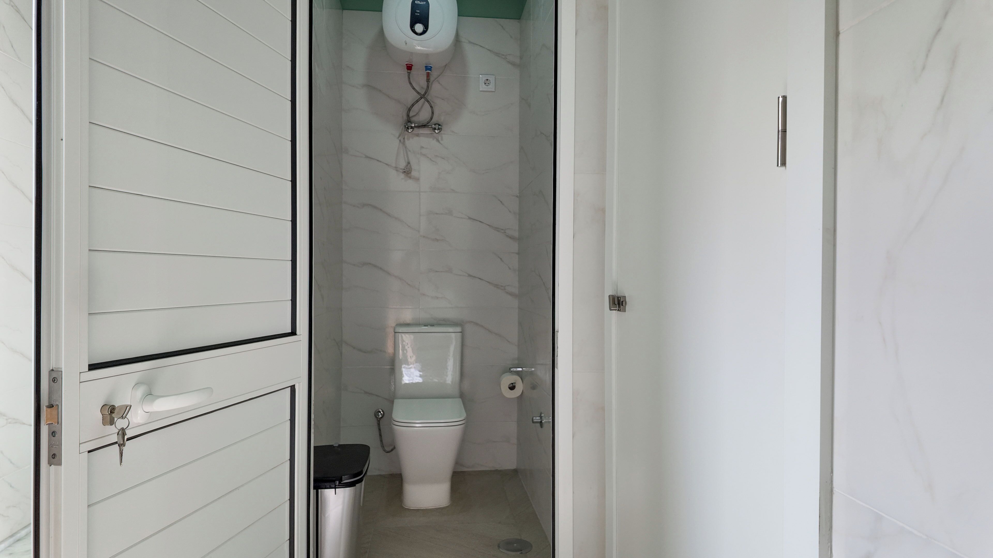 A bathroom with a toilet, a hand dryer, and a trash bin.