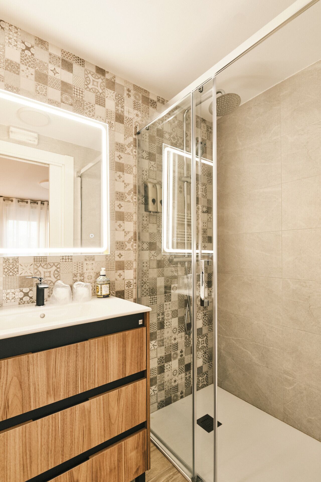 A bathroom with a wooden vanity, a glass shower enclosure, and patterned tiles.