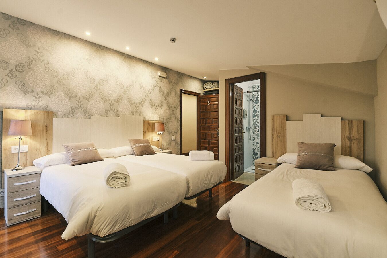 A hotel room with two beds, wooden headboards, a large mirror, and a shower area.