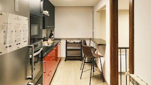 A modern kitchen with stainless steel appliances, a wooden chair, and a whiteboard on the wall.