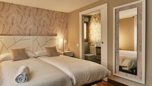 A hotel room with a large bed, a nightstand, a bedside lamp, a bathroom with a toilet and sink, and a large mirror.