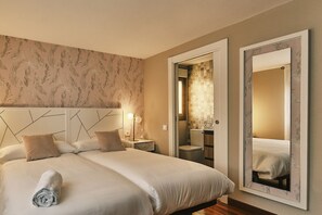 A hotel room with a large bed, a nightstand, a bedside lamp, a bathroom with a toilet and sink, and a large mirror.