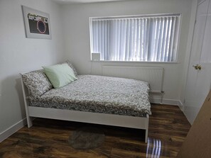 Ein Schlafzimmer mit einem Bett, einem Heizkörper, einem Fenster mit Jalousien und einem Bild an der Wand.