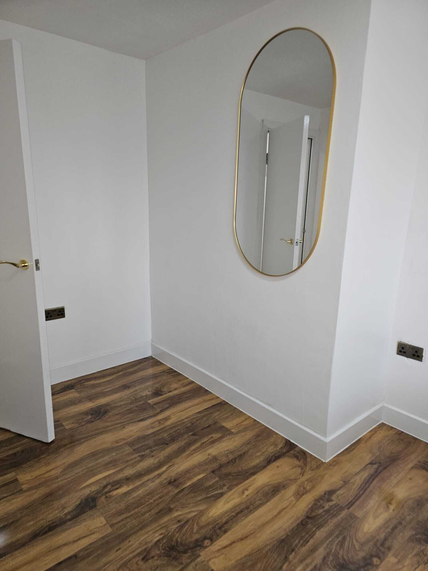 Ein Zimmer mit Holzboden, weißen Wänden und einem großen, ovalen Spiegel.