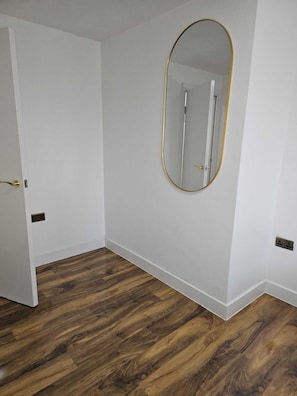 Ein Zimmer mit Holzboden, weißen Wänden und einem großen, ovalen Spiegel.
