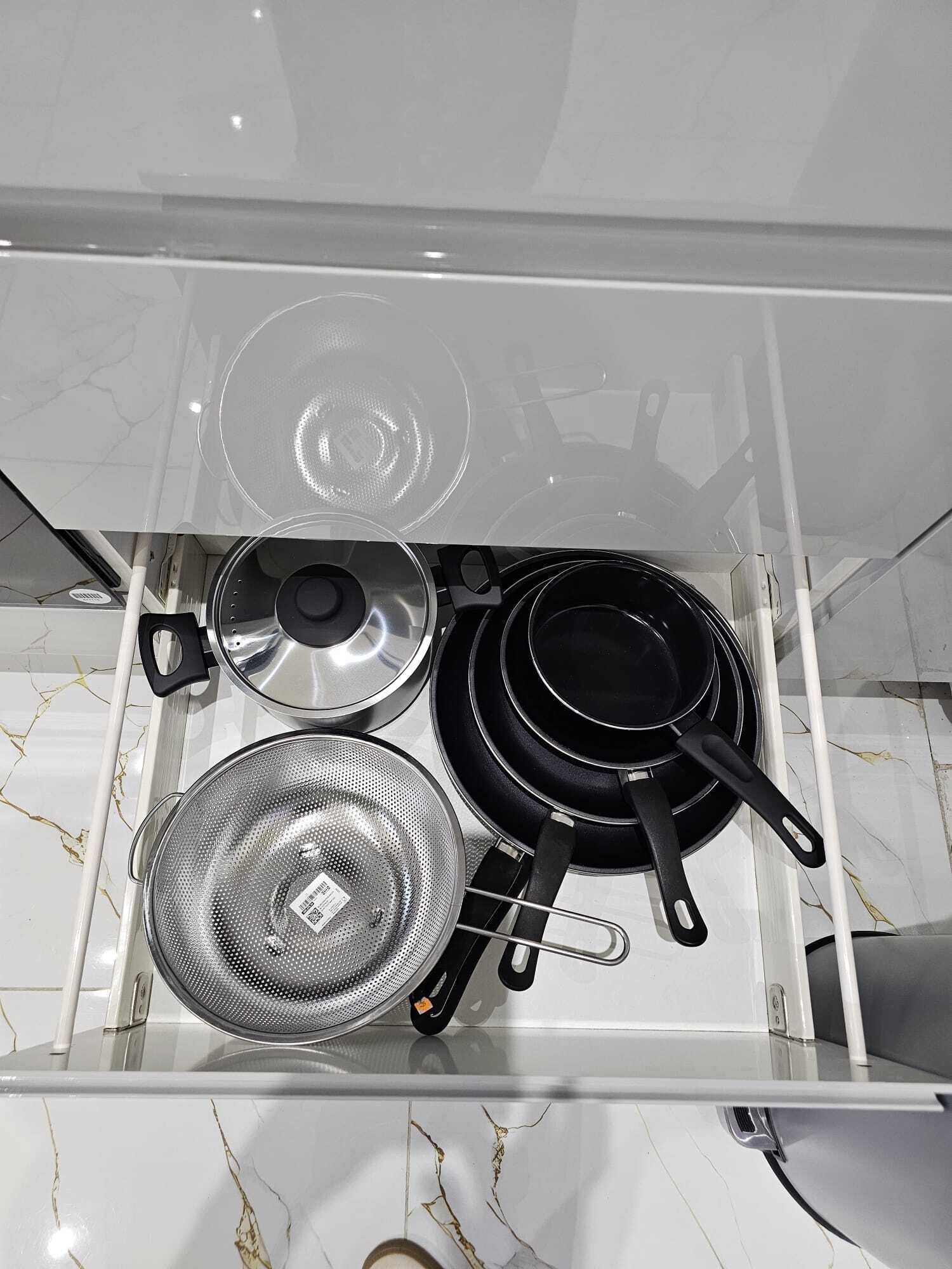 Una cocina con encimera de mármol blanco, estufa con ollas y sartenes, y un colador.