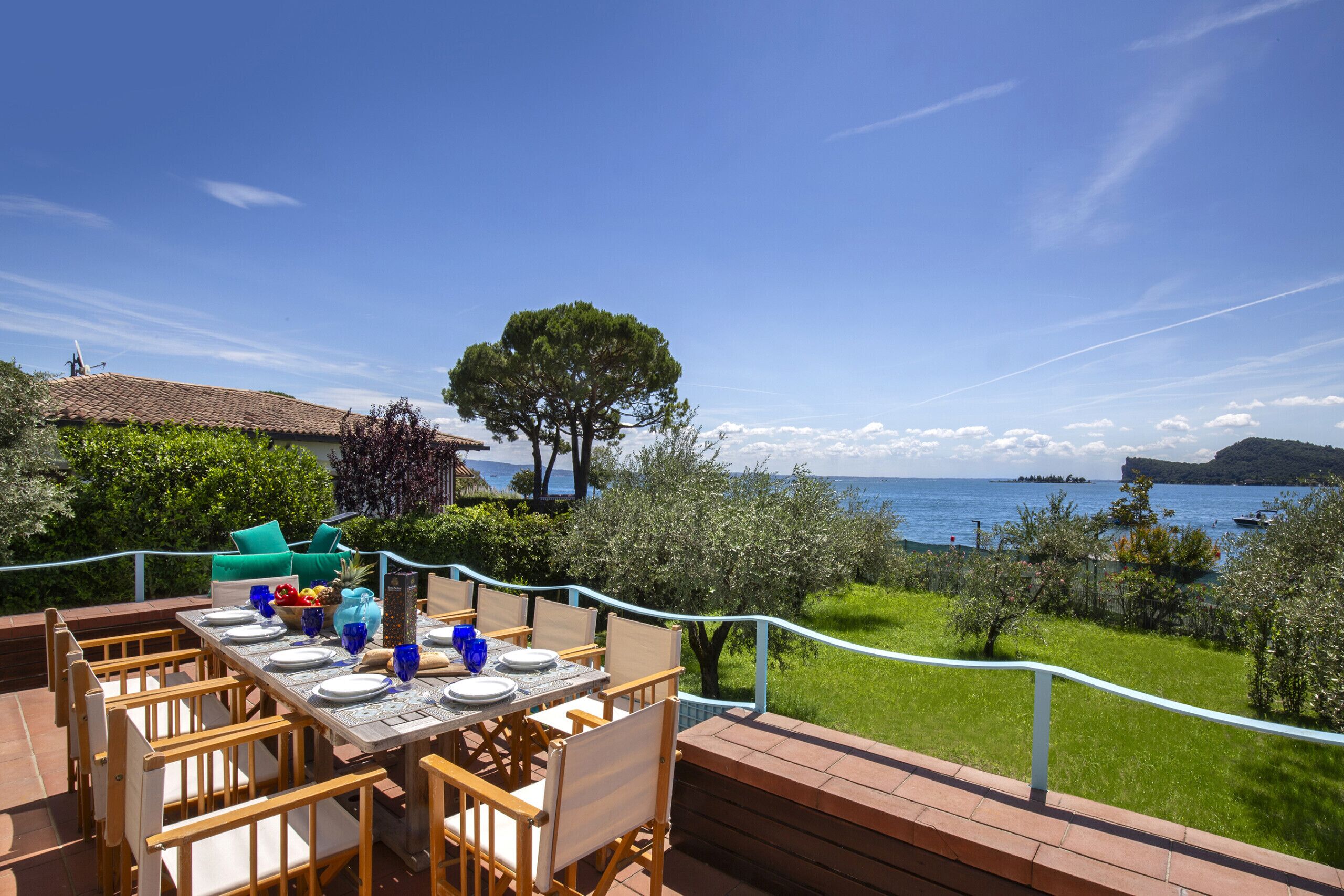 An outdoor dining area with a table set for four, overlooking a body of water and a mountainous landscape.