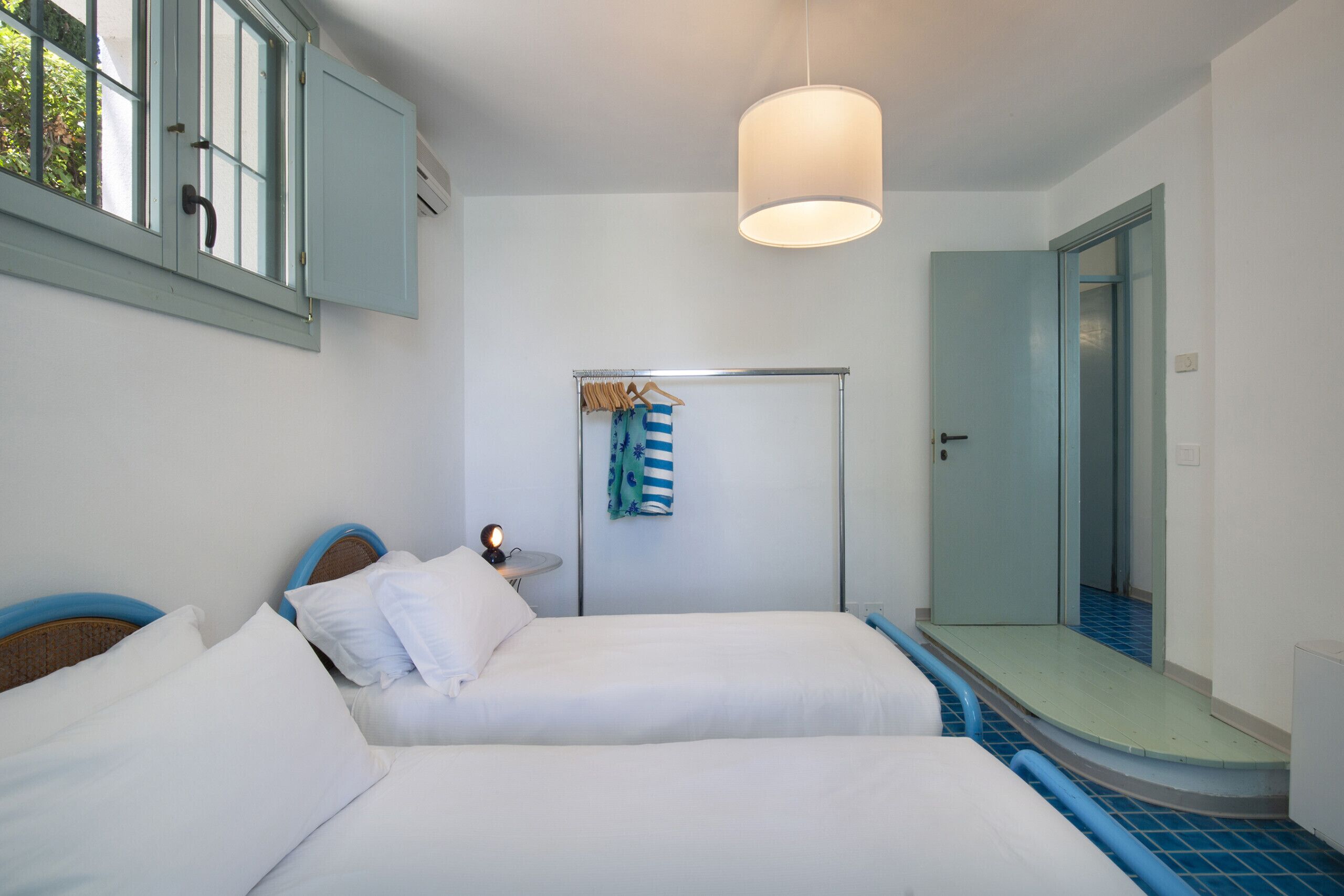 Ein Hotelzimmer mit zwei Betten, einem kleinen Tisch mit Lampe, einem Handtuchhalter mit Handtuch und einem Duschbereich.