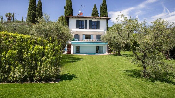 Ein zweistöckiges Haus mit Swimmingpool, umgeben von gepflegten Gärten und hohen Bäumen.