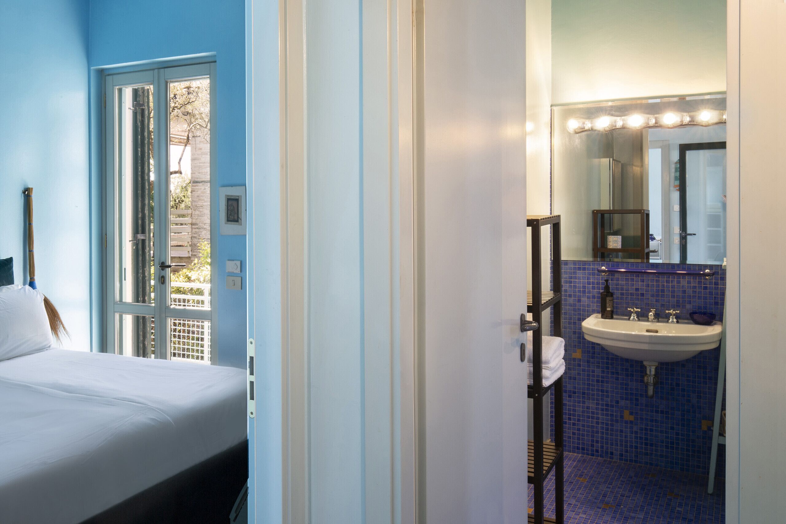 A hotel room with a bed, a bathroom with a sink and mirror, and a view of the outside.