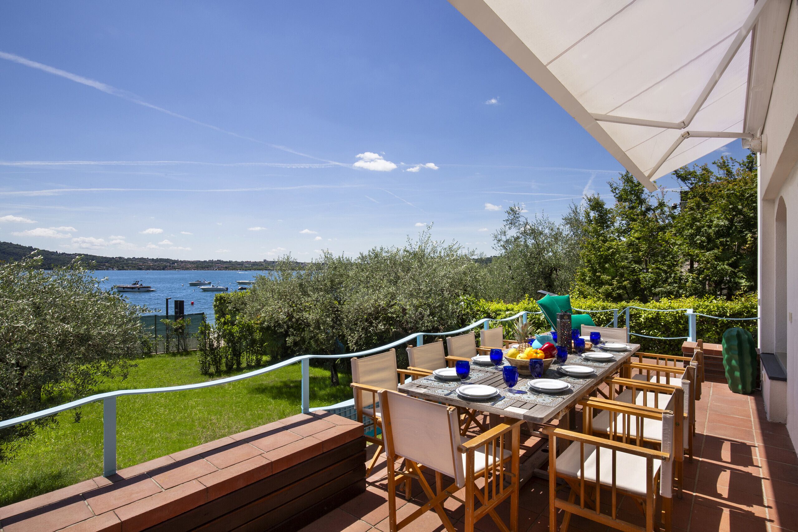 An outdoor dining area with a view of the sea and boats, wooden furniture, and a table set for two.