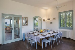 A dining area with a round table set for six, surrounded by six chairs, with a view of the outdoors through a window. - Villa Art with Private Pool (San Felice del Benaco)