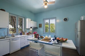 A kitchen with a central island, white cabinets, a stainless steel refrigerator, and a window with a view of greenery. - Villa Art with Private Pool (San Felice del Benaco)