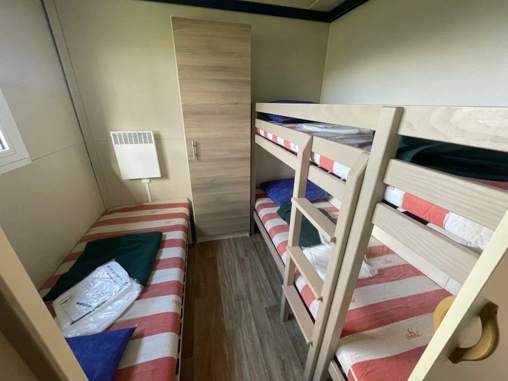 Een kleine, compacte kamer met stapelbedden, een raam en een wandairconditioner.