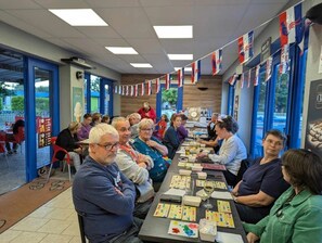 Eine Gruppe von Personen sitzt an einem langen Tisch in einem Raum mit blauen Fensterrahmen und Holzboden.