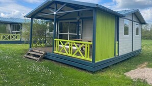 A single-story mobile home with a covered porch and a small deck, surrounded by a grassy area. - Chalet 3 étoiles - Piscine  - ccbgahi (Chatel-Chéhéry)