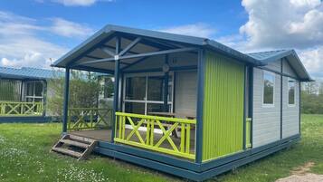 Une maison mobile de plain-pied, dotée d’un porche couvert et d’une petite terrasse, entourée d’une zone herbeuse.