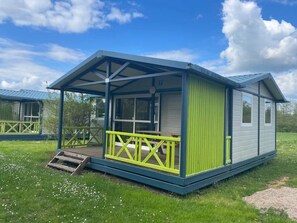 Een gelijkvloerse stacaravan met een overdekte veranda en een klein terras, gelegen in een gazon.