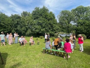 Een groep mensen is buiten bijeengekomen op een grasveld, met bomen op de achtergrond.