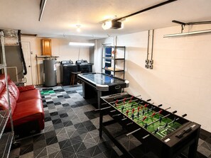Ein Zimmer mit Tischfußball, einem roten Ledersofa, einer Waschmaschine und einem Hauswirtschaftsraum mit Regalen.