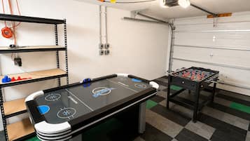 A room with a foosball table, a pool table, and shelves with various items.