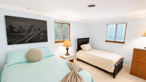 Um quarto com cama, mesa de cabeceira, abajur, cômoda e janela com persianas.