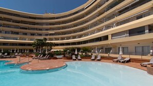 Een meerhoog hotel met een centraal gelegen zwembad, omringd door ligbedden en parasols.