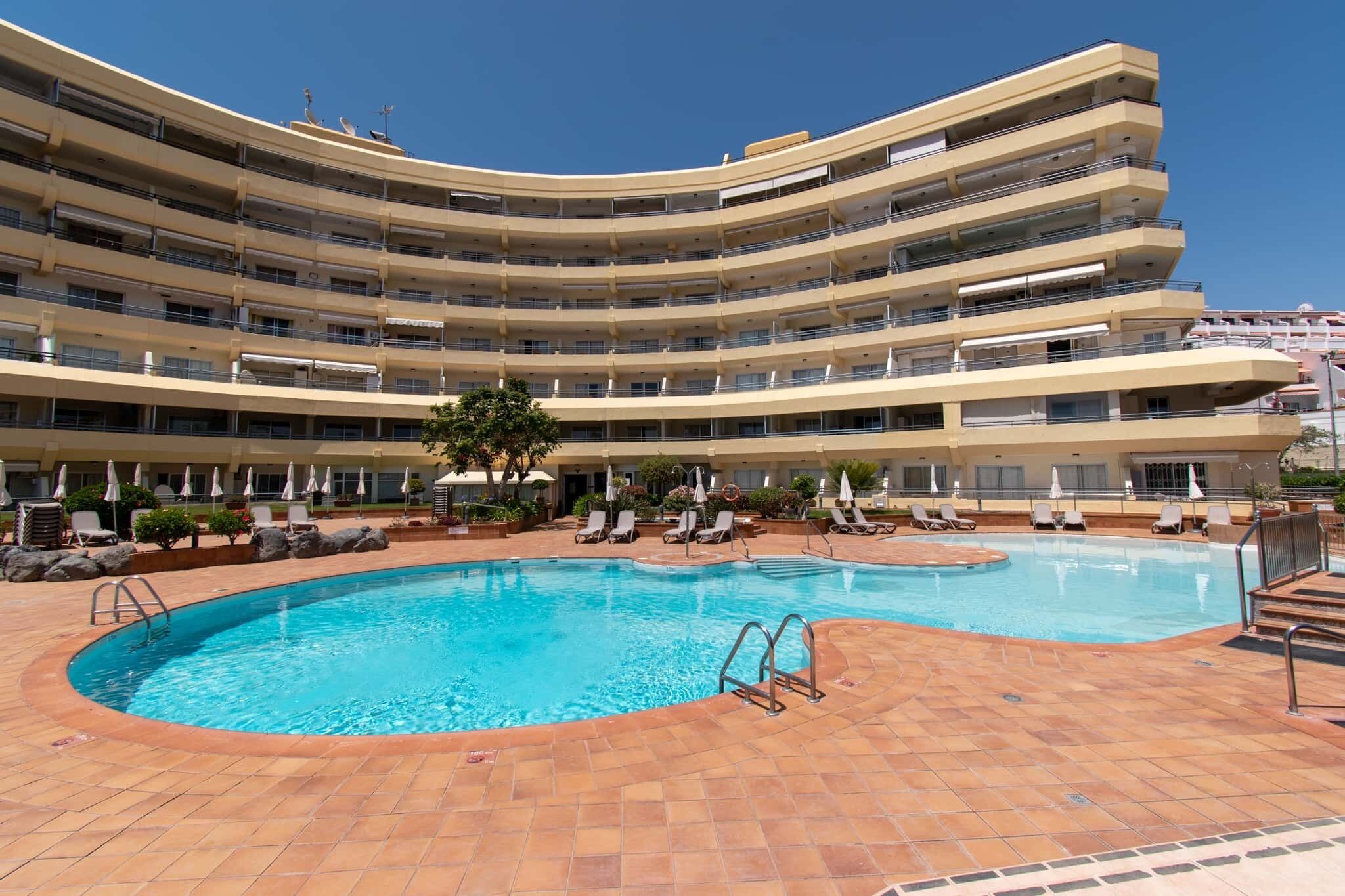 A multi-story hotel with a central swimming pool surrounded by sun loungers and umbrellas.