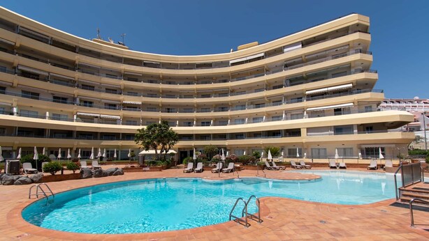 Een meerlaags hotel met een centraal gelegen zwembad, omringd door ligbedden en parasols.