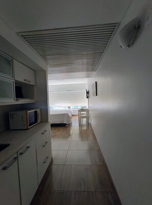 A narrow hallway leading to a bedroom with a bed, a chair, and a microwave on a cabinet. - Modern Apartment in Microcentro (Buenos Aires)