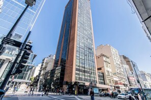 A tall modern building with a glass facade, surrounded by other buildings and a busy street scene. - Modern Apartment in Microcentro (Buenos Aires)