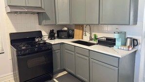 Uma cozinha compacta com armários cinza, um fogão preto, micro-ondas e cafeteira.