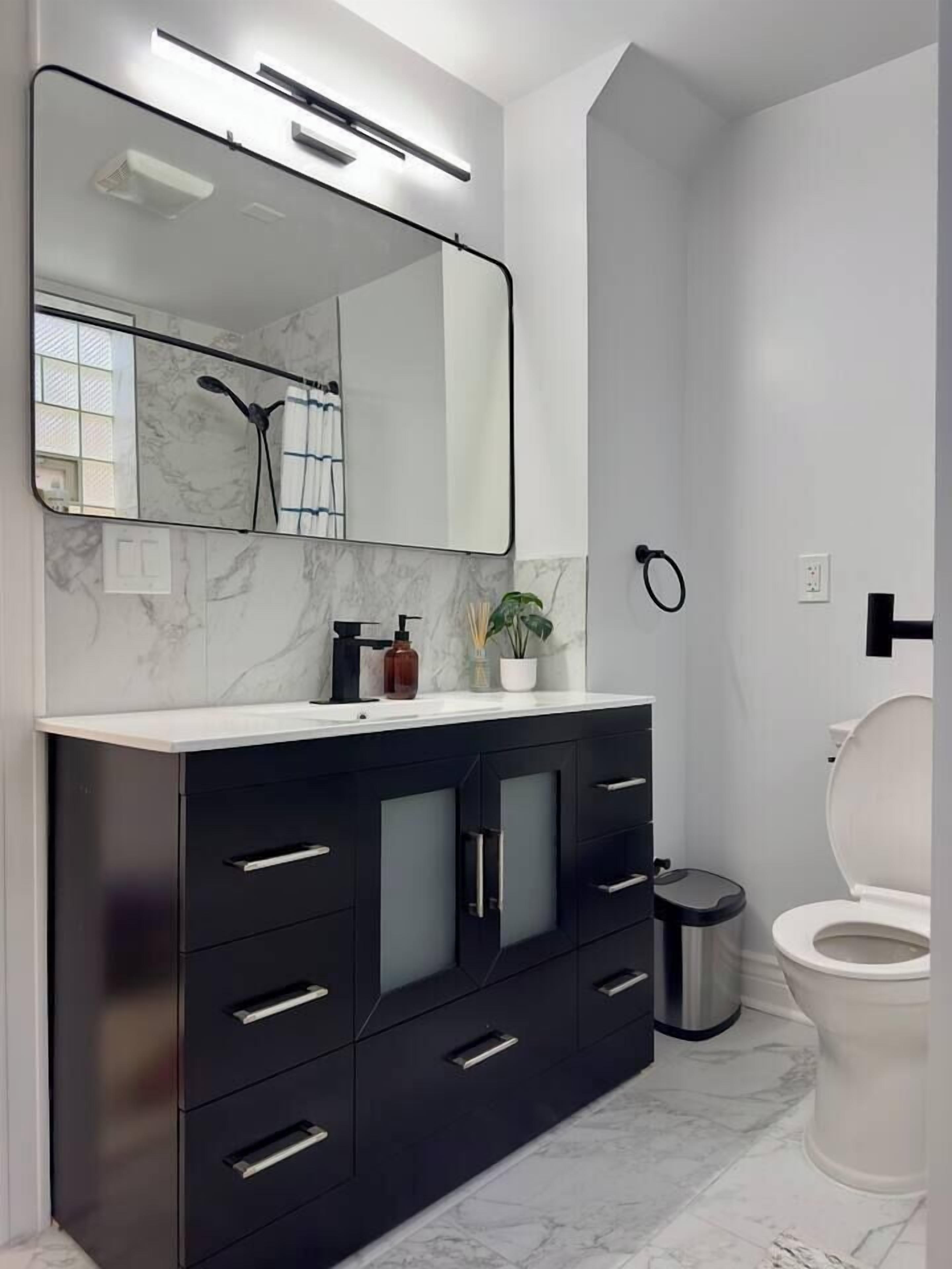 Uma casa de banho moderna com toucador preto, um espelho grande e uma sanita branca.