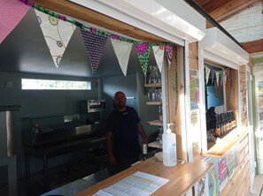 A kitchen area with a person standing behind a counter, a window, and various kitchen appliances.