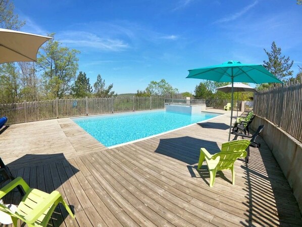 A wooden deck with a swimming pool, green chairs, and umbrellas.