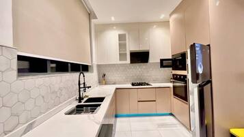 A modern kitchen with white countertops, a hexagonal tile backsplash, and built-in appliances including a stove, oven, and microwave.