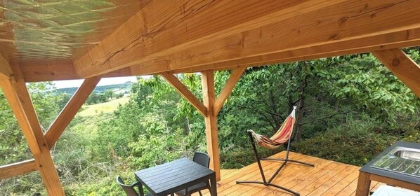 A wooden deck with a hammock, a table, and chairs.