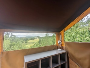 A room with a view of a green landscape through a window, a white desk lamp, and a wooden shelf.