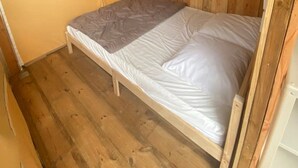 A single bed with a wooden frame in a room with wooden walls and a sloped ceiling.