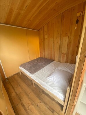 A single bed with a wooden frame in a room with wooden walls and a sloped ceiling.