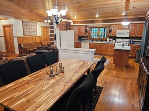 A modern kitchen with wooden cabinets, a central island, and a dining area with a wooden table and chairs. - Peaceful log cabin on large acreage with fire pit and private hiking trails. (Nashville)