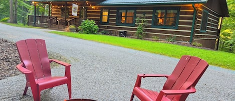 A cabin with a porch, red Adirondack chairs, and a fire pit.