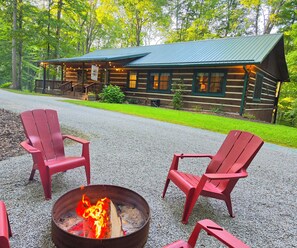 Une cabane avec une véranda, des fauteuils Adirondack rouges et un foyer extérieur.
