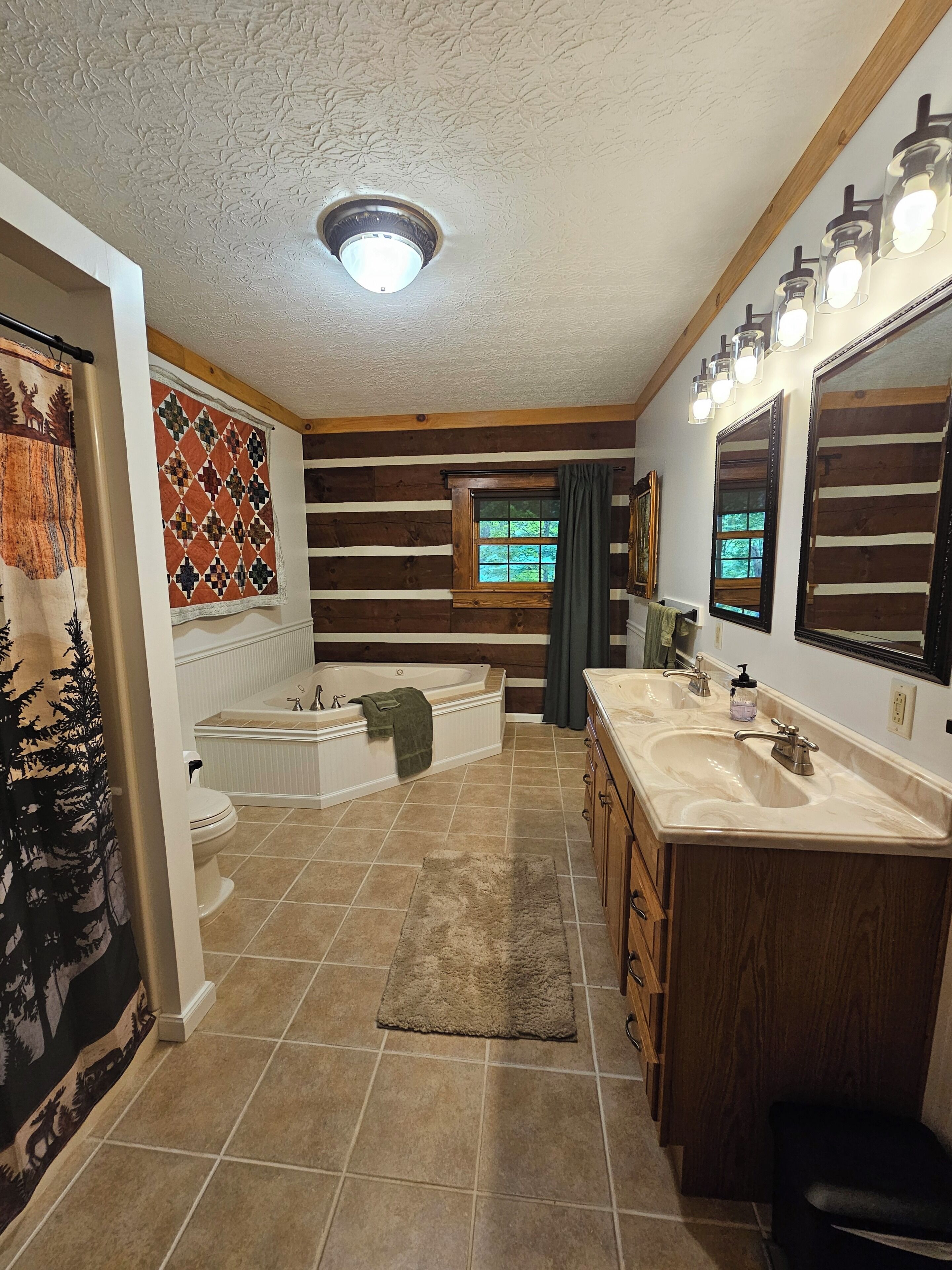 A bathroom with a bathtub, two sinks, a large mirror, and a window with curtains.